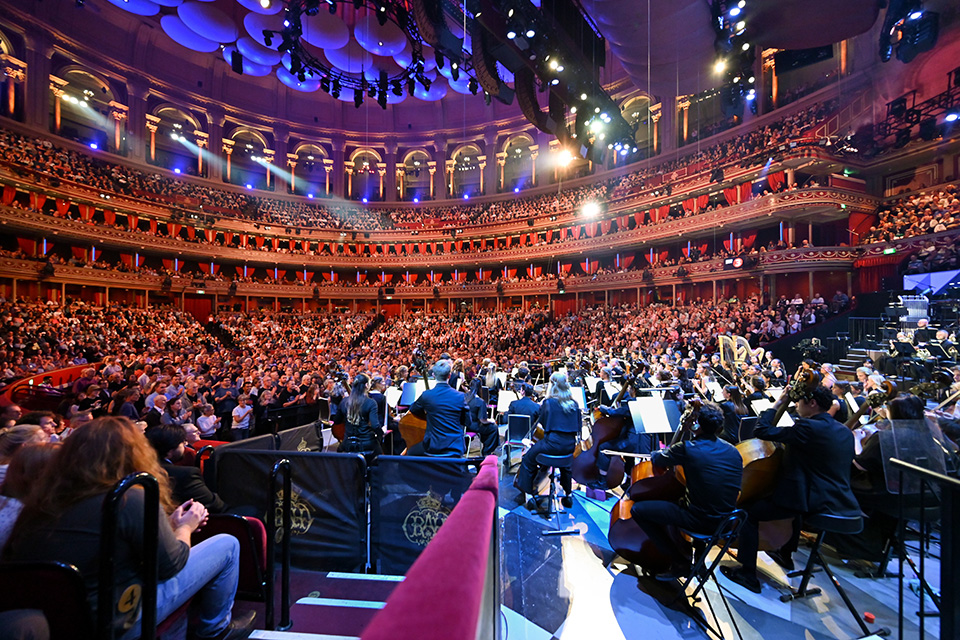 An orchestra all dressed in black with a packed out audience in a large round hall